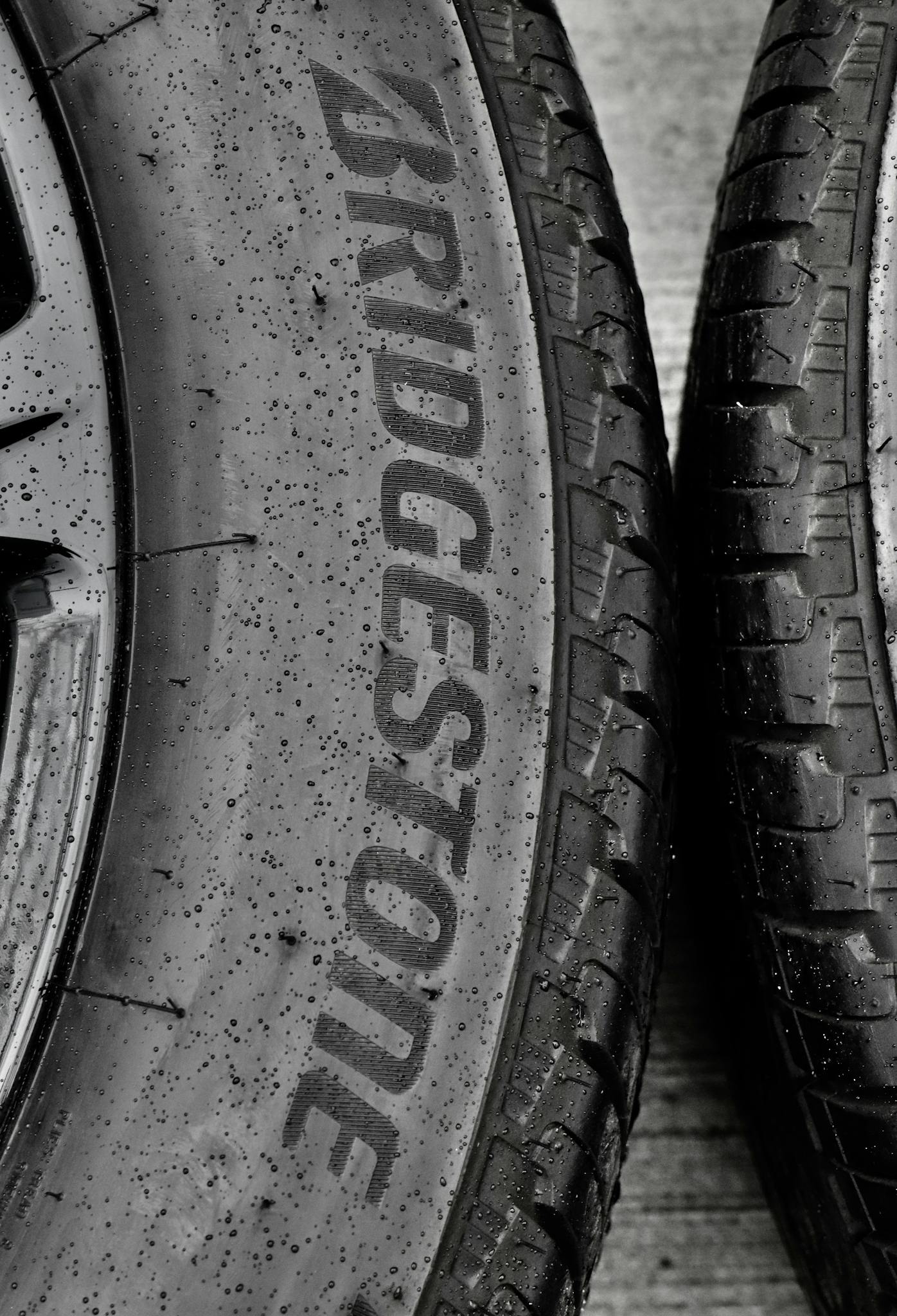 Detailed black and white close-up of wet Bridgestone car tires on asphalt.